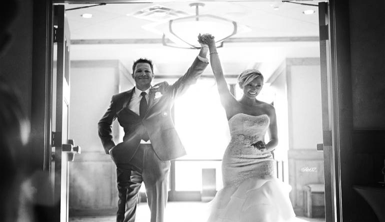 Νύφη και γαμπρός με τα χέρια ψηλά μπαίνουν σε εστιατόριο γάμου