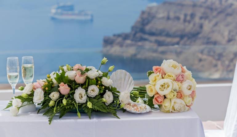Λουλούδια γάμου δίπλα σε δύο ποτήρια σαμπάνιας με θέα την ελληνική θάλασσα