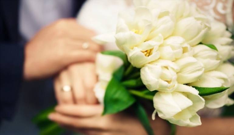 Ένα μπουκέτο από λευκές τουλίπες στα χέρια της νύφης και του γαμπρού.