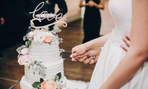 Ζευγάρι γάμου που κρατά το μαχαίρι και κόβει μαζί τη γαμήλια τούρτα διακοσμημένη με λουλούδια