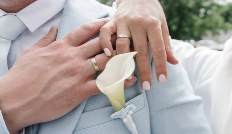 Χέρια νεονυμφών συζύγων με βέρες και λουλούδια για γάμο
