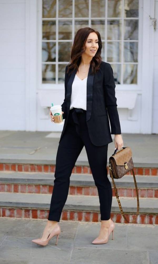 Γυναίκα περπατάει στον δρόμο πίνοντας καφέ και φορώντας μαύρο blazer